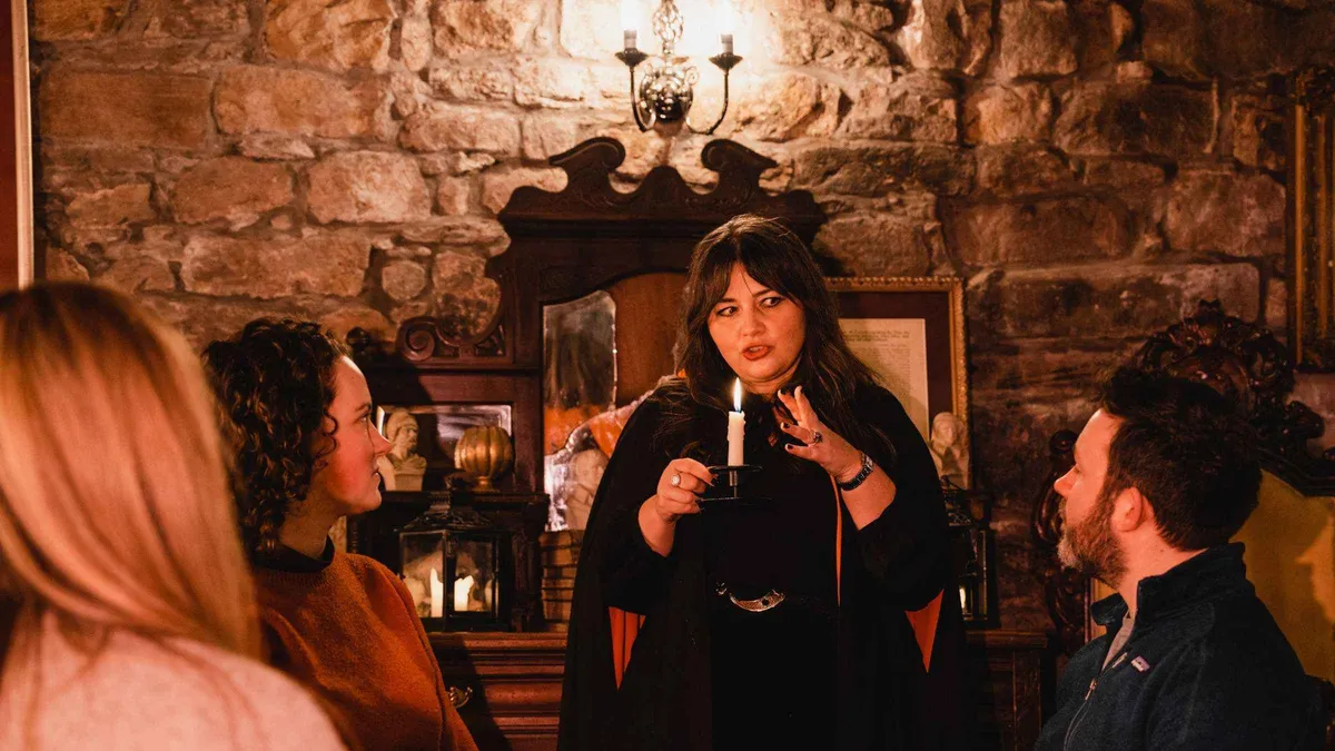 Storyteller guide with a small group at the Mercat Cross on an evening Edinburgh ghost tour with whisky, Royal Mile, Scotland