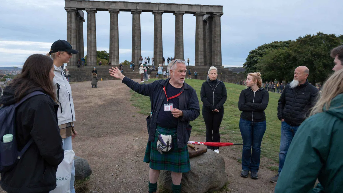 Guide with a red umbrella leading a group through Old Calton Burial Ground on an Edinburgh ghost tour, Calton Hill, Scotland